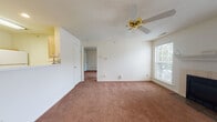 Located at 2000 N Linden St in Normal, Illinois, this single-floor unit offers a comfortable and functional layout. The living room serves as the heart of the space, featuring warm beige carpeting, a tile-surround fireplace with a white mantel, and a ceiling fan with a gold-toned fixture. Natural light flows in through windows with vertical blinds, and a front entry door with panel detailing provides a welcoming entryway. An adjacent carpeted area, also equipped with a ceiling fan and a large sliding glass door overlooking greenery, offers flexible use as a dining or secondary living space. A pass-through counter connects this area to the galley-style kitchen, which is outfitted with light wood cabinetry, white appliances including a range and refrigerator, a double basin sink, and tile flooring. The bathroom features a wood-trimmed vanity with white cabinet doors, a round basin sink, a large wall mirror, and tile flooring. Textured ceilings are consistent throughout the unit, and the neutral color palette of cream walls and earthy carpet tones creates a cohesive, move-in-ready atmosphere throughout the space.