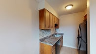 Located in Maplewood, this single-floor unit offers a practical and comfortable layout across several well-defined living spaces. The kitchen is efficiently designed with warm honey-toned wood cabinetry, dark granite-style countertops, a double stainless steel sink, and a tile backsplash that adds a decorative touch. Black appliances, including an electric range and over-the-range microwave, complete the cooking area. Light tile flooring runs throughout the kitchen and into the adjacent dining or transition area, which connects seamlessly to the carpeted living room. The living area is generously sized, featuring two horizontal windows that allow natural light to brighten the neutral-toned walls and plush carpet. A ceiling fan with integrated lighting provides both comfort and illumination. The bedrooms are similarly appointed with soft carpet, ceiling fans, and windows with blinds for privacy and light control. The full bathroom includes a single-sink vanity with white cabinetry, a mirror, wall-mounted lighting, and a tub-shower combination with tile surround in warm beige tones. Light tile flooring and neutral wall colors throughout the bathroom create a clean, cohesive look. Overall, the space presents a straightforward, functional design with consistent neutral finishes.
