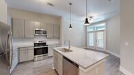 Located at 3915 William E Murray Blvd in Charleston, SC, this one-bedroom, one-bathroom unit offers a thoughtfully designed open floor plan with contemporary finishes. The kitchen serves as the centerpiece of the living area, showcasing a large island with a granite countertop and an undermount sink, complemented by taupe flat-front cabinetry, a subtle tile backsplash, and a full suite of stainless steel appliances including a refrigerator, range, microwave, and dishwasher. Pendant lighting above the island adds a refined touch, while light wood-look flooring extends throughout the main living space. A ceiling fan and access to a private balcony enhance the living area. The spacious bedroom features plush carpeting, a ceiling fan, and a window that brings in natural light with views of the outdoors. The bathroom is well-appointed with a double-sink granite vanity, taupe cabinetry with brushed nickel hardware, a glass-enclosed walk-in shower, and wood-look flooring that ties the design together. A hallway connects the rooms efficiently, and the unit includes an electrical panel for practical accessibility. The overall aesthetic is clean, modern, and move-in ready.