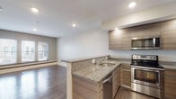 Located at 45 Bacon St in Watertown, MA, this single-floor unit offers a thoughtfully designed open-concept layout with a clean, contemporary aesthetic throughout. Hardwood flooring flows consistently across the living, dining, and bedroom areas, adding warmth and visual continuity to the space.

The kitchen is a standout feature, equipped with stainless steel appliances including a range, over-the-range microwave, and refrigerator. Flat-panel cabinetry in a warm woodgrain finish is paired with granite countertops that extend across a peninsula island, which incorporates an undermount sink and provides additional seating or workspace. Recessed lighting illuminates the kitchen area effectively.

The open living area is generously proportioned, benefiting from multiple windows that allow natural light to fill the room and offer views of the surrounding neighborhood. The bedroom areas are well-sized, with neutral-toned walls, hardwood floors, and ample natural light filtering through windows.

The bathroom is finished with coordinating granite vanity countertops, a woodgrain vanity cabinet, a large mirror, tile flooring, and a full tub-shower combination. The overall palette of the unit is neutral and modern, creating a cohesive and move-in-ready environment.