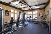 Located at 9150 S Coulter St in Amarillo, Texas, this fitness center is a well-equipped, single-floor facility designed to support a comprehensive workout routine. The space features soaring ceilings with exposed dark wood beams that lend a warm, architectural character to the room, while large multi-pane windows along the walls flood the interior with abundant natural light, creating an open and energizing atmosphere.

The cardio section is outfitted with multiple treadmills and elliptical trainers, positioned to take advantage of the natural light from the surrounding windows. The strength training area includes a multi-function cable and weight machine, a barbell rack with bench press setup, and a full dumbbell rack offering a range of free weights. Rubber flooring throughout provides durability and safety underfoot.

Additional amenities include exercise mats for stretching or floor work, a water cooler station stocked with hand sanitizer for hygiene, and a wall-mounted thermostat for climate control. Motivational framed prints — including "Hustle for That Muscle," "Witness the Fitness," and "Just Don't Quit" — are displayed throughout, contributing to an encouraging workout environment. Glass-paneled entry doors provide easy access, and posted fitness rules ensure a well-maintained facility for all users.