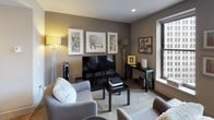 Located in the heart of Cleveland, OH, this thoughtfully designed single-floor residence offers a seamless blend of contemporary style and urban living. The open-concept kitchen is a standout feature, outfitted with flat-front wood cabinetry in warm tones, stainless steel appliances, a tiled backsplash, and a generous granite-topped island that serves as both a prep space and gathering spot. Stone-look tile flooring grounds the kitchen with a refined, durable finish. The living area provides a cozy yet sophisticated retreat, featuring warm neutral walls, recessed lighting, hardwood-style flooring, and a curated gallery wall arrangement that adds character to the space. Large windows allow natural light to filter in, enhancing the welcoming ambiance. The bedroom is a serene escape, highlighted by multiple windows that frame sweeping views of the Cleveland skyline and surrounding urban streetscape. Neutral carpeting and soft taupe walls contribute to its restful atmosphere. The bathroom is finished to a spa-like standard, featuring a floating vanity with granite countertops, backlit mirror, large-format tile walls and flooring, and a glass-enclosed walk-in shower, all combining for a sleek, luxurious feel. Throughout the residence, cohesive design elements and modern finishes create an atmosphere of refined urban comfort.