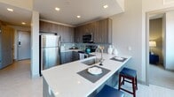 Located in the heart of downtown Rochester, NY, this contemporary single-floor residence offers a thoughtfully designed layout with modern finishes throughout. The open-concept kitchen is a standout feature, equipped with stainless steel appliances including a range, microwave, and dishwasher, complemented by rich wood-toned cabinetry, a sleek tile backsplash, and a generous quartz countertop island with bar seating — ideal for both cooking and casual dining. Light wood-style flooring runs through the main living areas, enhancing the bright, airy feel of the space. The living room offers a comfortable, versatile layout with large windows framing views of the Rochester skyline, allowing abundant natural light to fill the room. The bedroom provides a calm retreat, featuring plush carpeting, a double-door closet, and warm, neutral tones. A dedicated den or office space, also carpeted, includes a window with urban views and offers flexibility as a workspace or additional room. The bathroom is clean and efficiently designed with light flooring and modern fixtures. A full-length mirror near the entry adds a practical finishing touch. Throughout, the neutral color palette and contemporary design elements create a cohesive, polished urban living environment.
