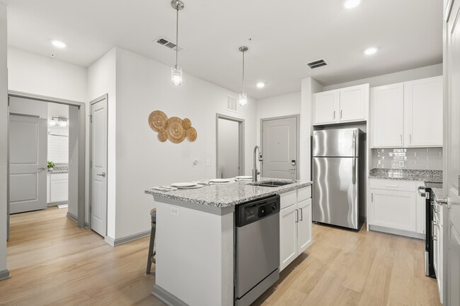 Modern kitchen with sleek granite countertops, stainless steel appliances, and inviting pendant lighting. - Avana Parkway