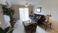 This single-floor residential space offers a comfortable and well-lit layout designed for everyday living. The living room serves as the heart of the home, featuring plush wall-to-wall carpeting that adds warmth underfoot. A ceiling fan with a light fixture is centrally mounted, providing both air circulation and ambient lighting. Large vertical blinds frame a sliding glass door that fills the room with natural light and offers a view to the outdoors, creating an open, airy atmosphere. The textured ceiling adds a classic touch to the overall aesthetic. The living area provides ample space for seating arrangements, making it well-suited for both relaxing and entertaining. Neutral wall tones throughout keep the space feeling clean and versatile, allowing for a variety of décor styles. The single-floor layout ensures seamless flow and easy accessibility across the entire living space. Overall, the residence combines functional design with comfortable living, highlighted by its inviting natural light, practical ceiling fan, and easy indoor-outdoor connection through the sliding glass door.