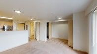 This single-floor residence offers a thoughtfully designed open-concept layout that seamlessly connects the kitchen and living area. The kitchen is well-equipped with stainless steel appliances, including a refrigerator, electric range, and dishwasher, all complemented by light maple cabinetry, ample counter space, and stone-patterned tile flooring. A raised breakfast bar divides the kitchen from the carpeted living area, which is bright and generously sized, served by recessed flush-mount lighting throughout.

The bedroom is a comfortable retreat, featuring plush carpeting, a large built-in closet with shelving and drawer storage, and a sliding glass door that opens to a private balcony overlooking a wooded outdoor view. Natural light fills the room through the floor-to-ceiling glass panel.

The bathroom is clean and functional, featuring a full tub and shower surround finished in crisp white tile. Additional storage is provided by a walk-in closet adjacent to the main living space. The entryway includes a dedicated electrical panel and keypad-secured entry door, adding a practical and secure touch to the home. Overall, the residence combines functional design with comfortable, neutral finishes throughout.