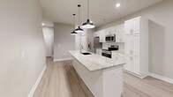 This well-designed two-storey home offers a thoughtful layout across two floors, delivering comfortable living in a clean, modern aesthetic. The main floor features an open-concept kitchen equipped with white shaker-style cabinetry, granite countertops, stainless steel appliances including a French door refrigerator, range, and over-the-range microwave. A central island with pendant lighting serves as a functional focal point. Light wood-look flooring runs throughout the main level, complementing the neutral warm-grey walls. A convenient half bathroom on this floor includes a pedestal sink, mirror, and modern fixtures. Carpeted stairs with a sleek metal railing lead to the upper floor.

Upstairs, two bedrooms are finished with plush carpet and neutral wall tones. The primary bedroom features a window with exterior views and direct access to a closet. Additional closet space is provided with wire shelving systems for organized storage. The upper level is served by two full bathrooms. Hallways connect all rooms efficiently. The overall interior palette of soft greiges, white trim, and light flooring creates a cohesive, contemporary feel throughout the home.