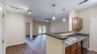 Located at 100 Ridgebrook Way NE in Atlanta, Georgia, this single-floor residence offers a thoughtfully designed open layout with consistent dark hardwood-style flooring throughout. The kitchen serves as a central hub of the home, featuring warm medium-tone wood cabinetry, dark granite-style countertops, a breakfast bar peninsula, and black appliances including a refrigerator and range. Pendant lights and track lighting illuminate the space, while a pass-through design opens seamlessly into the living area. The spacious living room is highlighted by a ceiling fan, neutral warm-toned walls, and glass French doors that lead to a private patio, bringing in natural light and views of mature trees and surrounding greenery. Multiple bedrooms offer a comfortable, versatile layout, each equipped with ceiling fans, natural light from windows with blinds, and generous floor space. The bathroom is well-appointed with a tiled tub-shower combination, a vanity with white cabinetry and a large mirror, and matching hardwood-style flooring. The kitchen also features a dedicated walk-in pantry or utility closet for added storage convenience. This residence delivers a clean, functional aesthetic throughout.