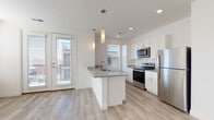 Located at 210 W Fifth Ave in Columbus, Ohio, this single-floor unit offers a thoughtfully designed layout with modern finishes throughout. The open-concept kitchen is a standout feature, showcasing white shaker cabinetry, granite countertops, stainless steel appliances including a range, microwave, and refrigerator, and a central peninsula with a undermount sink and pendant lighting above. Light wood-tone flooring runs throughout the main living areas, adding warmth and continuity to the space.

A bright hallway with a sliding barn door connects the living areas to the private quarters, which include generously sized bedrooms carpeted for comfort and fitted with large windows that allow ample natural light. Closet space is well accommodated, with at least one walk-in closet featuring wire shelving for organization.

The bathroom is appointed with a glass-enclosed walk-in shower, granite-topped vanity with white cabinetry, and wood-look tile flooring, complemented by brushed gold fixtures for an elevated aesthetic. A dedicated in-unit laundry closet houses a stacked washer and dryer, providing everyday convenience. The overall ambiance is clean, bright, and contemporary, making this a well-appointed space in the heart of Columbus.