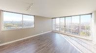 This single-floor unit is situated on an elevated level, offering sweeping city views through expansive floor-to-ceiling windows and a glass balcony door in the open-concept living area. The living space is generously proportioned, bathed in natural light, and finished with durable wood-look flooring that runs throughout the main areas, contributing to a clean, contemporary aesthetic.

The kitchen is thoughtfully designed with light wood-grain cabinetry extending to the ceiling for ample storage, white quartz countertops, a white subway tile backsplash, and a full suite of stainless steel appliances including a French door refrigerator, dishwasher, and range. A kitchen island with a pendant light above provides additional prep space and casual seating. Track lighting illuminates both the kitchen and the living area.

A hallway off the kitchen leads to the bedroom and bathroom. The bedroom is a well-sized, carpeted room featuring a mirrored sliding closet door alongside an additional closet with built-in shelving, offering plentiful storage. Neutral taupe walls create a calm, restful atmosphere. The bathroom includes a full soaking tub with a tiled surround and a curved shower rod, finished with chrome fixtures.