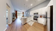 This thoughtfully designed single-floor residence offers a seamless blend of modern aesthetics and functional living. The open-concept kitchen and living area forms the heart of the home, highlighted by soaring vaulted ceilings and an abundance of natural light streaming through large windows. The kitchen is outfitted with crisp white shaker cabinetry, granite countertops, a peninsula island with a built-in sink, and a full suite of stainless steel appliances including a range, over-the-range microwave, dishwasher, and refrigerator. Stylish pendant lighting anchors the island, while wood-look flooring flows throughout the main living areas, adding warmth and continuity. The living area extends toward a large window with access to an outdoor space, enhanced by a ceiling fan overhead. The primary bedroom is a serene retreat, featuring plush carpet, tall ceilings, and generous windows that invite natural light. It connects to a large walk-in closet equipped with multi-tier wire shelving and hanging space. A secondary bedroom offers equal comfort with soft carpet and easy hallway access. The bathroom is finished with granite countertops, white cabinetry, wood-look flooring, and a tub-shower combination, completing this well-appointed residence.