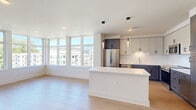 Located at 2105 Bond St in Charlottesville, VA, this thoughtfully designed residence offers three bedrooms and three full bathrooms across a well-appointed single-floor layout. The open-concept living and kitchen area serves as the heart of the home, featuring light hardwood flooring, clean white walls, and an expansive bank of floor-to-ceiling windows that flood the space with natural light and offer views of the surrounding Charlottesville skyline and greenery. The kitchen is outfitted with two-tone cabinetry — crisp white uppers and slate gray lowers — paired with quartz countertops, a classic subway tile backsplash, stainless steel appliances, and a central island ideal for dining or entertaining. A hallway connects the three bedrooms, each finished with the same warm hardwood flooring and neutral tones. The primary bedroom is a comfortable retreat with ample closet space. Each of the three bathrooms is finished with large-format tile flooring and surrounds, glass-enclosed showers, dark-accented vanities, and white quartz countertops, presenting a cohesive and modern aesthetic. The overall ambiance is bright, clean, and contemporary, making this Charlottesville residence a refined and functional living space.