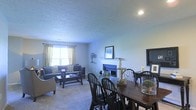 Located at 5400 Asherton Blvd. in Dublin, Ohio, this single-floor residence offers a comfortable and well-appointed living environment designed for both relaxation and everyday function. The open-concept layout seamlessly connects the living and dining areas, creating a cohesive and spacious feel throughout the main living space. The living area is anchored by a classic fireplace with a white mantel, serving as a natural focal point and adding warmth to the room. Plush wall-to-wall carpeting runs throughout, contributing to the cozy, inviting atmosphere. Large windows dressed with elegant curtains allow generous natural light to fill the space, brightening the neutral-toned walls and enhancing the overall ambiance. The dining area accommodates a full-sized dining table with seating for multiple guests, making it well-suited for entertaining. A textured ceiling adds a layer of architectural detail throughout. The thoughtful flow between living and dining zones makes the layout both practical and comfortable, ideal for day-to-day living in the Dublin, Ohio community.