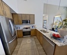 Located at 8020 Windrose Ave in Plano, Texas, this 890-square-foot single-floor apartment features 2 bedrooms, 2 bathrooms, 2 closets, and a hallway connecting the well-planned layout. Soaring ceilings throughout amplify the sense of space and airiness in every room. The open-concept kitchen and living area serves as the heart of the unit, featuring warm medium-tone cabinetry, granite countertops, stainless steel appliances including a gas range and French door refrigerator, a peninsula breakfast bar with pendant lighting, and light wood-style flooring. The living room benefits from dramatic floor-to-ceiling windows and a glass door leading to an outdoor balcony, flooding the space with natural light and offering exterior views. Both bedrooms are generously proportioned, with the primary bedroom spanning 130 square feet, and each features tall windows with ample natural light and dedicated closets. The two bathrooms are well-appointed with granite-topped vanities, warm wood cabinetry, subway-tiled tub-shower combinations, and wood-style flooring. The hallway provides seamless connectivity between rooms. Overall, the apartment presents a contemporary, upscale aesthetic with a cohesive neutral palette and high-quality finishes throughout.