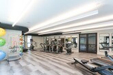 Located at 500 Ferguson Dr in Mountain View, California, this contemporary fitness center is designed to support a full range of exercise routines in a sleek, well-appointed environment. The single-floor facility features a spacious open layout with light wood-toned flooring that lends a clean, modern aesthetic throughout. Linear LED lighting runs across the ceilings, providing consistent, bright illumination that enhances the energetic atmosphere of the space. Large floor-to-ceiling windows along multiple walls invite abundant natural light and offer views of the surrounding outdoor environment, creating an airy feel. A dedicated cardio zone houses a row of Matrix elliptical trainers and treadmills, all equipped with individual display screens, as well as a rowing machine. Full-length mirrors line one wall, amplifying the sense of space and allowing users to monitor their form. A functional training area provides ample open floor space and includes a variety of accessories such as stability balls, resistance bands, medicine balls, and a water station. A wall-mounted television is positioned near the cardio machines for added convenience. The overall design balances a professional fitness environment with a clean, modern aesthetic, making it a well-rounded facility for everyday training needs.