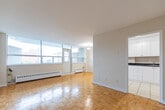 Located at 48 Grenoble Dr in Toronto's Don Mills neighbourhood, this 2-bedroom, 1-bathroom unit offers a practical and well-organized layout across a single floor. Classic parquet wood flooring runs throughout the main living areas, lending warmth and character to the space.

The open living and dining area is generously proportioned, bathed in natural light from a wide bank of floor-to-ceiling windows that frame views of the surrounding neighbourhood. A baseboard heating system lines the exterior walls beneath the windows, ensuring year-round comfort.

The kitchen is efficiently designed with white cabinetry, dark countertops, a tiled backsplash, and light tile flooring. It includes a white electric range and refrigerator, with ample upper and lower cabinet storage. A pendant light fixture illuminates the space, which opens directly toward the dining area.

The primary bedroom is a well-sized room featuring parquet flooring, a large window with outdoor views, and a double closet providing generous storage. The second bedroom is similarly bright, with a window and its own closet space.

The bathroom is finished with full-surround beige ceramic tile and includes a soaking tub with overhead shower. A hallway connects the main rooms, completing the unit's clean and functional flow.