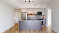 Located at 280 Montgomery Street in Ottawa, this modern two-bedroom, two-bathroom unit offers a thoughtfully designed open-concept layout spread across a single floor. Light hardwood flooring runs throughout, complementing the clean, contemporary aesthetic.

The combined living, dining, and kitchen area forms the heart of the space. The kitchen is outfitted with stainless steel appliances, including a refrigerator, gas range, built-in microwave, and dishwasher. White upper cabinetry is paired with warm wood open shelving and grey lower cabinets, accented by a grid-pattern tile backsplash. A substantial kitchen island with a stone countertop provides additional workspace and casual seating.

Large floor-to-ceiling windows in the living area flood the space with natural light and frame impressive views of the Ottawa River, surrounding greenery, and the city skyline beyond.

Both bedrooms are bright and well-proportioned. The primary bedroom features a mirrored sliding-door closet and expansive windows with sweeping outdoor views. The second bedroom is equally airy with its own closet.

The two bathrooms are finished in a modern palette — one features floor-to-ceiling white vertical tile in the tub surround, while the other includes a built-in vanity with grey cabinetry and tiled walls. Additional conveniences include in-unit laundry, an entrance, a hallway, and three closets throughout.