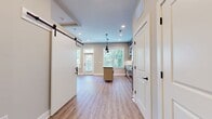 This efficiently designed 630 square foot space maximizes functionality in a single-floor layout. The interior showcases a contemporary aesthetic with light-colored walls that enhance the sense of openness. A standout feature is the stylish barn door, adding a modern farmhouse touch while serving as a space-saving solution. The flooring throughout is a durable wood-look material, likely vinyl or laminate, offering warmth and easy maintenance. Recessed lighting in the ceiling provides even illumination. The open concept design seamlessly integrates the kitchen and living areas, promoting a spacious feel despite the compact square footage. Multiple electrical outlets are visible, indicating thoughtful consideration for modern living needs. The closet, while not visible in the image, adds valuable storage to the compact layout. This space is ideal for those seeking a minimalist, low-maintenance living environment with a touch of modern design.