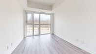 This contemporary 2-bedroom, 1-bathroom unit offers a well-designed open-concept layout finished with light wood-style laminate flooring throughout. The kitchen is efficiently arranged along one wall, featuring warm wood-tone cabinetry, a tiled backsplash, and a full suite of stainless steel appliances including a refrigerator, dishwasher, microwave, and electric range — all illuminated by overhead track lighting. The kitchen flows seamlessly into a bright, spacious living area with clean white walls and an open, airy feel. The primary bedroom is a comfortable, well-proportioned room highlighted by large floor-to-ceiling sliding glass doors that open to the outdoors and fill the space with natural light, offering views of the surrounding greenery. A built-in sliding door closet provides ample storage. The second bedroom is equally bright with its own sliding door closet and convenient access to the kitchen area. A dedicated entryway with an additional closet provides a functional transition into the unit. The full bathroom is finished with large-format floor tiles, a wood-tone floating vanity with a white countertop, a mirrored medicine cabinet, and a tiled tub-shower combination. In-unit stacked laundry is also conveniently located adjacent to the bathroom.