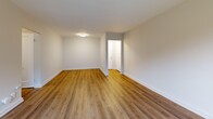 This 2-bedroom, 1-bathroom residence offers a clean, modern aesthetic across a well-organized single-floor layout. Warm hardwood-style flooring runs throughout, complemented by crisp white walls and white trim, creating a bright and cohesive feel from room to room.

The spacious living room is a standout feature, offering generous proportions with large windows that invite abundant natural light and views of surrounding greenery. A dedicated entrance and hallway provide a practical transition into the main living areas.

The kitchen is equipped with stainless steel appliances, including an electric range and an over-the-range microwave, set against white cabinetry and a classic subway tile backsplash. A window above the counter brings in natural light and views of the landscaped grounds outside.

Both bedrooms are comfortably sized, each featuring large windows with radiator heating units beneath them, ensuring warmth and bright views of the surrounding neighborhood. The primary bedroom offers a notably generous footprint with ample room for furnishings.

The bathroom is finished in all-white tile with a full soaking tub, shower, vanity with sink, and a window for natural ventilation. Throughout the residence, radiator heating is present in multiple rooms, reflecting a classic and reliable building infrastructure paired with contemporary updates.