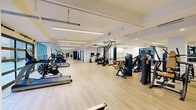 Located at 1020 N Tyndall Ave in Tucson, Arizona, this expansive fitness center offers a generously sized, single-floor layout designed to accommodate a wide range of exercise needs. The space is bathed in natural light, thanks to floor-to-ceiling glass windows and doors that line the perimeter, providing open views of the surrounding area and creating an inviting, energizing atmosphere.

The interior features clean white walls, light wood flooring, and modern linear LED lighting, all contributing to a bright and contemporary aesthetic. Large wall-to-wall mirrors in the cardio section visually expand the space and allow users to monitor their form during workouts.

The fitness floor is comprehensively equipped with a robust lineup of cardio machines, including treadmills, stair climbers, ellipticals, stationary bikes, and rowing machines. The strength training area houses a full array of selectorized resistance machines, cable systems, free weights, dumbbells, and functional training tools such as medicine balls and stability balls. A dedicated boxing bag station adds a combat fitness option to the facility.

Garage-style glass doors open to an adjacent outdoor area, seamlessly connecting the interior workout space to the outside. The layout flows thoughtfully across distinct exercise zones, offering ample room for movement. The facility's polished design and extensive equipment selection make it a well-appointed destination for fitness.
