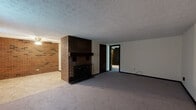 Located at 55–65 Industrial Dr in Ellington, Connecticut, this single-floor unit presents a practical and characterful layout with several notable architectural details throughout. The spacious living area is anchored by a freestanding brick fireplace that serves as a central focal point, complemented by an exposed brick accent wall that adds warmth and texture to the space. Plush wall-to-wall carpeting runs through the living and bedroom areas, while a textured ceiling is consistent throughout. A sliding glass door floods the living space with natural light and provides direct views of the outdoors, enhancing the sense of openness. The kitchen is well-appointed with warm wood cabinetry, a double sink, a white electric range, a refrigerator, and tile flooring, with an exposed brick wall continuing the design theme from the main living area. The bedroom offers a quiet, carpeted retreat with a window that allows natural light, a dark-stained wood door, and baseboard heating. The bathroom features a full tub and shower, a white vanity with medicine cabinet, tile flooring, and a striking exposed brick wall that ties the space cohesively to the rest of the unit. Baseboard heating is present throughout, and the overall layout is efficiently organized for comfortable single-floor living.