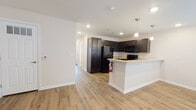 This single-floor residence offers a thoughtfully designed layout that balances functionality and modern style throughout. The open-concept kitchen and living area serves as the heart of the unit, where light wood-look flooring extends seamlessly underfoot. The kitchen is equipped with dark espresso cabinetry, light stone-tone countertops, and black appliances including a refrigerator, electric range, and microwave. A peninsula with pendant lighting above provides a natural divide between the kitchen and the adjacent living space, creating an ideal area for casual dining or entertaining. The living room features a ceiling fan with light kit and direct access to the front entry door, which is framed with a sidelight panel to allow natural light to filter in. The bedroom is generously sized, also featuring a ceiling fan and a window fitted with blinds for privacy and light control. The bathroom is finished with neutral tile flooring, a full tub and shower surround clad in white square tile, a dark vanity with stone-tone countertop, and brushed nickel fixtures throughout. Clean white walls and recessed lighting throughout the unit contribute to a bright, welcoming ambiance that feels both contemporary and comfortable.