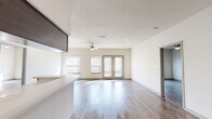 This thoughtfully designed 2-bedroom, 2-bathroom single-story residence features a contemporary open-concept layout that seamlessly connects the kitchen, dining, and living areas. The kitchen is a standout feature, boasting rich dark-walnut cabinetry, light quartz countertops, stainless steel appliances including a range, microwave, and dishwasher, and elevated ceilings with track lighting that add a sense of height and drama. A peninsula island provides additional counter space and a natural division between the kitchen and living areas. The expansive living room is bathed in natural light from large windows and a set of glass French doors that open to the outdoors, complemented by a ceiling fan overhead. Wood-style flooring runs consistently throughout the entire residence, adding warmth and visual continuity. Both bedrooms are generously sized, each with access to dedicated closets featuring wire shelving systems that maximize storage. The primary bedroom includes a spacious walk-in closet. Each bathroom is cleanly appointed, with one featuring a tiled tub-shower combination, wood-tone vanity cabinetry, and wood-style flooring. The overall ambiance is bright, clean, and modern, offering a comfortable and functional living environment.