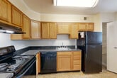 Located at 38 N Summit Dr in Gaithersburg, MD, this single-floor, one-bedroom, one-bathroom home offers a thoughtfully organized layout across a comfortable footprint. The open living and dining areas are finished with neutral-toned carpet and cream walls, creating a bright, welcoming atmosphere. A ceiling fan with light fixture anchors the living room, which receives natural light through a front-facing window. The spacious bedroom features plush carpeting, a large window overlooking lush greenery, and direct access to the full bathroom. The bathroom is finished with classic gray tile surrounding a full soaking tub and shower combination, complemented by a vanity with a white countertop. The kitchen is well-appointed with warm oak cabinetry extending to the upper walls, dark granite-style countertops, tile flooring, a skylight overhead, and black appliances including an electric range, dishwasher, and refrigerator. Crown molding adds a refined touch. The home also includes a den, a hallway, and three closets, providing generous storage throughout. The neutral color palette and carpeted living spaces lend the home a clean, move-in ready feel.
