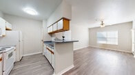 This single-floor residence offers a practical and comfortable layout across two bedrooms and two bathrooms. The open-concept kitchen and living area serves as the heart of the home, featuring a peninsula with dark granite-style countertops that separates the kitchen from the living space. The kitchen is equipped with white cabinetry accented by warm wood trim, matching white appliances including a range, microwave, and refrigerator, and a stainless steel sink. Wood-look laminate flooring runs throughout the main living areas, adding a clean, cohesive feel. The living room benefits from a ceiling fan and a window that brings in natural light. A hallway connects the main living area to the private quarters, where two bedrooms feature plush carpeting, ceiling fans, and windows with blinds. The primary bedroom includes direct access to its own bathroom. Both bathrooms are finished with wood-trimmed cabinetry, granite-style countertops, and tiled tub-shower combinations. Two closets and a dedicated laundry area provide ample storage and convenience. Neutral tones and white trim throughout lend the space a bright, move-in-ready appeal.