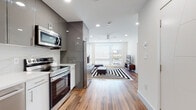 This contemporary single-floor residence showcases a thoughtfully designed open-concept layout connecting the kitchen and living area seamlessly. The kitchen is a standout feature, outfitted with high-gloss gray upper cabinetry, crisp white lower cabinets, and a striking marble-style backsplash. Stainless steel appliances — including a refrigerator with water dispenser, electric range, built-in microwave, and dishwasher — complement the sleek quartz countertops. Warm wood-look flooring runs throughout the space, adding natural texture to the modern palette.

The living area is bathed in natural light from a large window, and a ceiling fan adds comfort. Two well-proportioned bedrooms provide restful retreats, each featuring the same warm hardwood flooring, clean white walls, and ceiling fans for airflow.

The bathrooms are finished to an impressive standard, with floor-to-ceiling marble-style porcelain tile creating a luxurious, spa-like atmosphere. One bathroom features a frameless glass sliding shower enclosure over a soaking tub, while the other includes a white vanity with under-sink storage and recessed lighting. Together, the rooms create a cohesive, modern aesthetic that balances style with everyday functionality.