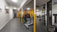 Located at 1865 N Fuller Ave in the heart of Los Angeles, this fitness center offers a generously proportioned, single-floor workout space designed to accommodate a wide variety of exercise needs. The layout is open and functional, with yellow accent columns and walls providing a bold, energizing aesthetic that contrasts with the clean white walls and ceiling throughout the main area.

The space is well-lit with recessed and flush-mounted ceiling lights, creating a bright and inviting atmosphere. Durable rubber flooring covers the entire area, offering both safety and comfort underfoot. Full-length mirrors line one wall, visually expanding the room while allowing users to monitor their form during workouts.

The fitness center is comprehensively equipped, featuring a multi-station cable and pulley strength machine, a rack of free weights and dumbbells, benches, and a rowing machine. A dedicated cardio zone, highlighted by the vibrant yellow walls, houses a treadmill, ellipticals, a stationary bike, and an inversion table. The space also includes a ceiling fan for added air circulation in the cardio area.

Colorful artwork adorns the walls, lending a touch of personality to the environment. A secured exit door with clearly marked emergency signage ensures safety. Overall, this fitness center combines practicality with an upbeat design to deliver a complete on-site workout experience.