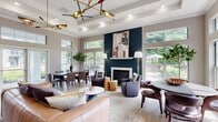 Located at 1623 Parkridge Cir in Crofton, Maryland, this single-floor community space offers a thoughtfully designed, open-concept layout that seamlessly blends comfort and contemporary style. The main gathering area commands attention with soaring tray ceilings adorned with a striking brass mid-century modern chandelier, adding a sculptural focal point overhead. Light hardwood flooring runs throughout, contributing to a warm and cohesive aesthetic.

The living and lounge area centers around a dramatic floor-to-ceiling dark navy shiplap fireplace wall with a classic white mantle and herringbone tile surround, serving as the room's architectural anchor. An abundance of oversized windows and glass doors flood the interior with natural light while offering views of the surrounding greenery.

The space accommodates multiple seating and dining arrangements, making it well-suited for both social gatherings and quiet retreats. A dedicated kitchen features bold navy cabinetry with gold hardware, a curved white quartz island with bar seating, a chevron-patterned tile backsplash, and glass-front upper cabinets — delivering both function and design sophistication. French doors provide additional access points, enhancing the flow between indoor and outdoor areas. Crown molding and recessed lighting complete the polished, upscale character of this well-appointed community space.