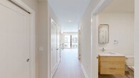Located at 922 N Broad St in Philadelphia's vibrant Francisville neighborhood, this thoughtfully designed single-floor unit offers an efficient and modern layout across a well-utilized footprint. The open-plan kitchen and living area serves as the heart of the space, featuring light wood cabinetry that extends to the ceiling for ample storage, stainless steel appliances including a refrigerator, range, and microwave, a white subway tile backsplash, and light-toned countertops. Light hardwood flooring runs throughout, contributing to a bright, cohesive aesthetic. The living area benefits from large sliding glass doors that open directly onto a private balcony, flooding the space with natural light and providing outdoor access with views of the surrounding neighborhood. A central hallway connects the living spaces to two well-appointed bathrooms, each featuring warm wood vanities with clean white countertops and marble-style tile flooring. Two closets provide generous storage, while a dedicated laundry area adds everyday convenience. Recessed lighting throughout and a neutral warm-white color palette give the entire unit a clean, contemporary feel. The space is well-suited for those seeking modern finishes and practical functionality in a prime Philadelphia location.