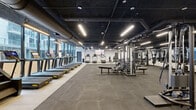 This expansive 4,950 square foot fitness center in Miami showcases a cutting-edge blend of form and function. The space boasts an industrial-chic aesthetic with exposed ductwork, concrete floors, and a mix of white brick and gray walls. Large windows flood the area with natural light, offering city views and creating an open, airy atmosphere.

The facility is divided into distinct zones, each catering to different workout needs. A spacious cardio area features a row of treadmills and other machines facing large windows and a wall-mounted TV. The strength training section is equipped with a comprehensive array of weight machines and free weights. A functional fitness area includes TRX straps and open floor space for dynamic exercises.

The center's design incorporates modern lighting fixtures, including LED strips that accentuate the industrial ceiling. Artistic wall graphics add visual interest and energy to the space. The layout promotes easy flow between different workout areas, while maintaining a sense of openness throughout the facility.

Storage solutions for fitness accessories and user belongings are seamlessly integrated into the design. The overall ambiance strikes a balance between a sleek, contemporary gym and a raw, urban workout space, appealing to fitness enthusiasts who appreciate both style and substance in their exercise environment.