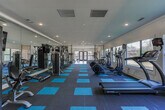 Located at 304 N Colonial Homes Circle NW in Atlanta, Georgia, this single-story fitness center offers a thoughtfully designed workout facility divided into two functional zones. The main exercise area features distinctive charcoal and teal modular flooring, providing a modern, energetic aesthetic throughout the space. Large windows line the perimeter walls, flooding the interior with natural light and offering views of the surrounding greenery, creating an inviting atmosphere for exercise.

The primary zone houses an impressive array of cardio equipment, including multiple elliptical trainers and treadmills, complemented by a full cable-based strength training system. Floor-to-ceiling mirrors along one wall visually expand the space while allowing users to monitor their form during workouts. Recessed lighting supplements the natural light, ensuring consistent illumination throughout.

A secondary zone, finished with light hardwood-style flooring, provides a more versatile workout area equipped with additional treadmills, free weights, kettlebells, medicine balls, and a rowing machine. Glass double doors in this section open directly to the outdoors, enhancing ventilation and connectivity to the exterior. Together, both zones create a comprehensive, well-lit fitness environment suitable for a wide range of training styles.