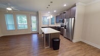 This well-designed single-floor residence offers a cohesive blend of modern finishes and functional living spaces throughout. The open-concept kitchen serves as the heart of the home, showcasing rich dark-toned cabinetry, crisp white countertops, and a full suite of stainless steel appliances including a French door refrigerator, range, built-in microwave, and dishwasher. A central island with a sleek white surface provides additional prep space and casual seating, while pendant lighting above adds a refined touch. Recessed lighting and crown molding throughout the kitchen and living areas elevate the overall aesthetic.

Warm hardwood-style flooring flows seamlessly across the main living areas, complementing the neutral wall tones. The living area benefits from natural light streaming through large windows with views of lush greenery, and a ceiling fan adds both comfort and style. Bedrooms are generously proportioned, each featuring hardwood-style floors, ceiling fans, and bright windows. One bedroom includes access to a walk-in closet.

The bathroom is finished with a rich dark wood vanity, granite-style countertop, undermount sink, and a backlit mirror that creates an elegant ambiance. The dedicated laundry room accommodates a full-size washer and dryer, adding everyday convenience to this thoughtfully appointed residence.