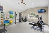 Located at 16340 Lasselle Street in Moreno Valley, CA, this fitness center is a well-appointed, single-floor facility thoughtfully divided into two connected rooms. The space features vaulted ceilings that lend an open, airy feel, complemented by large arched and rectangular windows that flood the interior with natural light and offer views of the surrounding outdoor area.

The main exercise room is equipped with a comprehensive selection of cardio machines, including treadmills, stationary bikes, and elliptical trainers, each positioned on protective floor mats. A wall-mounted flat-screen TV provides entertainment during workouts. A ceiling fan keeps the space comfortable, while recessed lighting ensures visibility throughout.

An adjoining room serves as a dedicated strength and free-weight area, featuring a multi-station cable machine, a weight bench, a full dumbbell rack, and a storage rack holding an assortment of stability balls and resistance accessories. Mirrored walls enhance the sense of space and support proper form during exercise.

The entry area includes seating and posted fitness center rules. Glass double doors open directly to an outdoor patio and pool area, seamlessly connecting the indoor facility with the exterior amenities. Light-toned flooring and neutral walls throughout create a clean, motivating environment for users of all fitness levels.