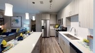 This single-floor residence showcases a cohesive contemporary design throughout its living spaces. The kitchen serves as a functional centerpiece, featuring stainless steel appliances including a French door refrigerator, electric range, microwave, and dishwasher. Light wood-grain cabinetry lines the walls floor-to-ceiling, complemented by white quartz countertops, a tiled backsplash, and a large island with pendant lighting overhead. Track lighting provides additional illumination across the workspace.

Multiple bedrooms offer distinct personalities while maintaining a consistent aesthetic. One features a dramatic tufted gray upholstered headboard, ceiling fan, and a large window with drape panels allowing ample natural light. Another bedroom incorporates decorative wall-mounted planters and pendant lighting, while a third showcases a patterned valance above white horizontal blinds. All bedrooms feature wood-look flooring and neutral gray walls.

The unit includes two bathrooms. One offers a walk-in glass-enclosed shower with clean white surround panels, while the second provides a full tub-shower combination with a white tile surround. Both bathrooms feature wood-look flooring, neutral taupe walls, and understated décor, maintaining the unit's modern and cohesive design throughout.