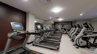 Located at 51 N High St in the heart of Columbus, Ohio, this fitness center offers a well-appointed and fully equipped workout facility designed to meet the needs of serious exercisers. The space is anchored by a row of modern Matrix treadmills and elliptical machines, providing ample cardio options for guests or members. Large mirrored walls line one side of the room, visually expanding the space and allowing users to monitor their form during workouts. A striking black-and-white vintage-style mural depicting athletic figures adorns the far wall, adding a dynamic and energetic aesthetic to the environment. The facility is finished with light-colored flooring that contrasts cleanly with the darker equipment, contributing to a bright and motivating atmosphere. Recessed and overhead lighting ensures the space is well-illuminated throughout. The layout is thoughtfully organized, with equipment arranged to allow for comfortable circulation and use. The clean, modern interior design reflects a professional standard consistent with the building's prominent downtown Columbus address, making this fitness center a functional and visually engaging space for daily exercise.
