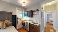 This single-floor residence offers a thoughtfully designed layout highlighted by warm hardwood flooring throughout. The kitchen serves as a central feature, showcasing dark walnut-toned cabinetry, white quartz countertops, and a striking herringbone-patterned white tile backsplash. Stainless steel appliances, including a range, dishwasher, and refrigerator, complement the space, while open shelving adds both function and style. A peninsula with a quartz countertop provides additional workspace and connects seamlessly to the living area, which benefits from multiple windows offering views of surrounding greenery and generous natural light.

The two bedrooms are finished in neutral gray tones with hardwood floors and windows framing outdoor foliage. Each room includes closet access and baseboard heating. The full bathroom features classic white square floor tile, a full-size tub with tiled surround, and a pedestal-style sink, maintaining a clean and timeless aesthetic. Throughout the unit, white trim, flush-mount lighting, and a consistent neutral palette create a cohesive, understated ambiance suited to comfortable everyday living.