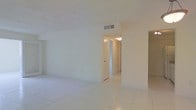 This single-floor space presents a clean, minimalist aesthetic throughout, characterized by bright white walls and smooth tile flooring that reflect light and create a sense of openness. The main living area is generously proportioned, offering a flexible, open layout that can be easily adapted to suit a variety of needs and furnishing arrangements. Neutral tones dominate the interior palette, lending the space a calm and welcoming ambiance. A central hallway connects the living area to additional rooms, providing a logical and functional flow throughout the unit. Ceiling-mounted HVAC vents are integrated discreetly, ensuring comfort without disrupting the clean lines of the space. Interior doors are finished in white to complement the overall design, maintaining a cohesive and uncluttered look. The tile flooring, consistent across the visible areas, is easy to maintain and contributes to the bright, airy feel of the interior. Overall, this space offers a straightforward, well-lit environment with a neutral canvas ideal for personalization.