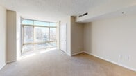 Located at 1215 E West Hwy in Silver Spring, Maryland, this single-floor residence offers a thoughtfully designed open layout that maximizes both functionality and comfort. The living area is generously proportioned, featuring plush neutral carpeting, a textured ceiling, and track lighting that adds a modern touch. A standout feature is the expansive floor-to-ceiling window wall that floods the space with natural light while offering sweeping views of the surrounding Silver Spring urban skyline.

The kitchen is seamlessly integrated into the living space via a peninsula-style breakfast bar topped with dark granite countertops, providing a natural divide while maintaining an open feel. Inside the kitchen, light maple cabinetry lines the walls, complemented by matching granite countertops, tile flooring, and a full suite of black appliances including a gas range, built-in microwave, dishwasher, and refrigerator. A skylight-style ceiling fixture provides bright, even illumination throughout the cooking area.

The bathroom is clean and functional, featuring white tile flooring, a large vanity mirror, and crisp white fixtures. A hallway with multiple closeted storage spaces connects the main living areas, adding practical convenience. The overall aesthetic is neutral and move-in ready, with a bright, airy ambiance enhanced by the abundant natural light throughout.