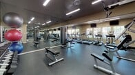 Located at 6400 Bell St in Amarillo, Texas, this fitness center offers a comprehensive, single-floor workout facility designed to support a wide range of exercise routines. The space is thoughtfully laid out to accommodate both cardio and strength training, with clearly defined zones for each type of activity.

The cardio area features multiple treadmills, elliptical machines, and a stationary bike, all positioned in front of large windows that allow natural light to fill the room and provide views of the surrounding outdoor greenery. Wall-mounted televisions are positioned overhead for entertainment during workouts.

The strength training section is outfitted with cable machines and weight benches, supported by full-length mirrors along the walls that enhance the sense of space and allow users to monitor their form. A dedicated free weights area includes a comprehensive dumbbell rack with a wide range of weights, medicine balls, and an assortment of stability and exercise balls neatly stored on racks.

Throughout the facility, dark rubberized flooring provides both durability and safety. Recessed and overhead fluorescent lighting ensures bright, even illumination across the entire space. The neutral-toned walls and mirrored surfaces create an open, functional ambiance well-suited for focused fitness activity.