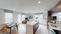 This single-floor residence showcases a thoughtfully designed open-concept layout that seamlessly connects the kitchen, dining, and living areas. The kitchen is outfitted with rich dark wood cabinetry extending to the ceiling, light quartz countertops, a full suite of stainless steel appliances, and a subway tile backsplash. A large central island with dark cabinetry provides additional prep space and storage, while light hardwood-style flooring runs throughout the main living areas.

The open living and dining space is bright and welcoming, benefiting from multiple windows dressed with roman shades and blinds that allow ample natural light. The living area offers comfortable space for seating and entertainment, while the dining area accommodates a full table for gatherings.

An entry hallway features a built-in slatted wall panel with hooks, offering practical organization upon arrival, alongside access to additional storage. Two well-proportioned bedrooms are carpeted and receive natural light through large windows with ceiling fans overhead. The bathroom is finished with a distinctive patterned tile floor, a floating dark wood double vanity with white countertops, and a large mirror with vanity lighting.