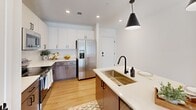 Located at 720 River Hwy in Mooresville, NC, this well-appointed single-story home offers three bedrooms, two bathrooms, and a thoughtfully designed open-concept layout. The kitchen is a standout feature, showcasing a two-tone cabinet design with crisp white uppers and warm taupe lowers, a classic subway tile backsplash, stainless steel appliances, and a large center island with a quartz countertop and a matte black faucet over a deep undermount sink. Striking black pendant lights anchor the space, which flows seamlessly into the living area featuring light wood-style flooring and a ceiling fan. French doors in the living room invite natural light and provide outdoor access. The bedrooms are carpeted and bright, each equipped with ceiling fans and multiple windows with exterior views. The primary bedroom is generously sized with ample closet space. The primary bathroom features warm wood-tone cabinetry, a white quartz vanity, a walk-in glass shower, and light hardwood-style flooring. The secondary bathroom includes a shower/tub combination, wood-tone flooring, and a bright window. Clean white walls and modern black hardware fixtures create a cohesive, contemporary aesthetic throughout the home.