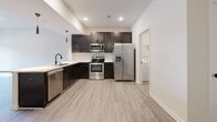 This single-story home in Clarksville, Tennessee, offers a well-designed open-concept layout that seamlessly connects the main living and kitchen areas. Light gray wood-look flooring flows throughout the common spaces, complementing the neutral color palette and recessed lighting overhead. Ceiling fans are present throughout, adding to the home's comfort and functionality.

The kitchen is a standout feature, equipped with rich dark espresso cabinetry, crisp white countertops, and a full suite of stainless steel appliances — including a side-by-side refrigerator with ice and water dispenser, electric range, over-the-range microwave, and dishwasher. A pendant light adds a subtle decorative touch above the sink area, which overlooks the open living space.

The bedrooms are carpeted for warmth and comfort, each with ceiling fans and ample natural light. At least one bedroom includes a walk-in closet with built-in shelving, offering generous storage. The bathroom features a tub-shower combination with tiled surround, light wood-look flooring, and matte black hardware accents.

A dedicated laundry room houses a full-size washer and dryer and includes overhead wire shelving. The home also features a front entry area with a ceiling fan and a louvered closet door, providing additional storage near the entrance.