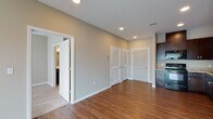 This single-floor residential unit offers a thoughtfully designed open-concept layout that seamlessly connects the main living areas. The kitchen is a functional and stylish centerpiece, featuring rich dark-wood cabinetry, granite-look countertops, black Whirlpool appliances including an electric range, over-the-range microwave, dishwasher, and a double-basin sink. Warm hardwood-style flooring extends throughout the kitchen and main living and dining areas, lending a cohesive and inviting feel to the space.

The living area is generously proportioned, illuminated by recessed lighting and a large sliding glass door fitted with vertical blinds that fill the room with natural light. A utility closet with louvered doors and additional storage are conveniently located near the entry hallway, along with a visible electrical panel.

The bedroom offers plush carpeting, a ceiling fan with light fixture, and a window providing additional natural light. The bathroom is well-appointed with a dark-wood vanity, marble-look countertop with an integrated sink, a large mirror, and a separate walk-in closet accessible directly from the bathroom. Neutral warm-gray wall tones throughout the unit create a calm and versatile backdrop suited to a variety of interior styles.