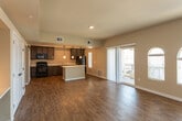 This single-story residence at 780 W Cherry Ln in Carlsbad, New Mexico, offers a thoughtfully designed open-concept layout with a seamless flow between the living and kitchen areas. Rich wood-look plank flooring extends throughout the main living spaces, complemented by warm, neutral-toned walls that create an inviting atmosphere. The expansive living room is highlighted by elegant arched windows that flood the space with natural light, a ceiling fan, and a sliding glass door that opens to an outdoor patio area. The kitchen is a standout feature, showcasing dark espresso cabinetry, light countertops, a central island with pendant lighting, black appliances, and a stylish barn door leading to additional storage. Recessed lighting adds a modern touch overhead. The bedrooms offer plush wall-to-wall carpeting, ceiling fans, and multiple windows with blinds that allow for adjustable natural light. The bathroom features warm wood-look flooring, a dark-framed vanity mirror, a single-sink vanity with dark cabinetry, and built-in shelving for added convenience. The overall design balances functionality with a clean, contemporary aesthetic throughout this comfortable single-floor home.