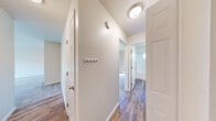 This single-floor residence offers a thoughtfully designed layout that balances functionality and comfort throughout its interconnected spaces. The kitchen is outfitted with white shaker-style cabinetry, dark gray countertops, and stainless steel appliances including a range, microwave, and dishwasher. A window with plantation shutters allows natural light to brighten the workspace, while wood-look flooring adds warmth underfoot.

A central hallway connects the main living areas, featuring wood-look flooring, neutral painted walls, a ceiling-mounted light fixture, and a built-in wall hook rack for added convenience. The hallway provides access to the bedroom spaces and bathroom.

The bedrooms are carpeted and finished in soft neutral tones. One bedroom features a sliding glass door opening to a private balcony with outdoor views of mature trees, while another offers a large window with similar views and direct balcony access. A spacious closet with a standard rod is found in one of the bedrooms.

The full bathroom includes a white vanity with dark countertop, an undermount sink, a mirrored medicine cabinet, and a tub and shower combination enclosed by sliding frosted glass doors. A small window provides natural ventilation.

The living area is carpeted and bright, anchored by a sliding glass door that opens to an outdoor space with views of surrounding greenery.